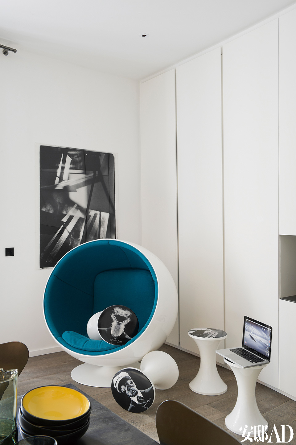房间一角摆放着由Eero Aarnio设计的蓝白色玻璃纤维球形椅(Fiber Ball Chair)，散落的带有黑白图片的几只小凳子是摄影师和设计师Maurice Renoma对Tam Tam凳的再设计。