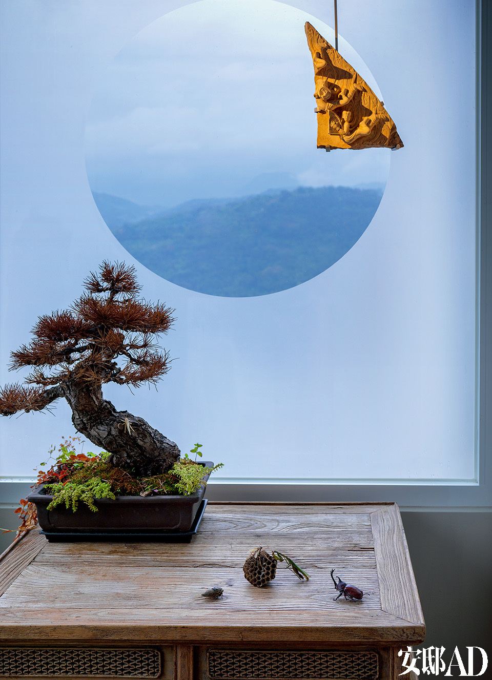 玄关处特意设置了中国园林的圆窗借景的效果，能直视户外的山景变化。明中期的木桌上摆着一个枯松盆景，上悬北齐时代的飞天石刻，以表示对来客的欢迎。