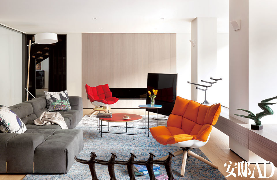 位于一层的另一个小客厅里，设计感十足的家具与艺术品成为主角。红色与橘色座椅来自B&B Italia,灰色沙发同样来自B&B Italia，名为Tufty-Too，白色落地灯来自Roll & Hill，架子上的枝形烛台来自Tom Dixon，以上物品均购于家天地。