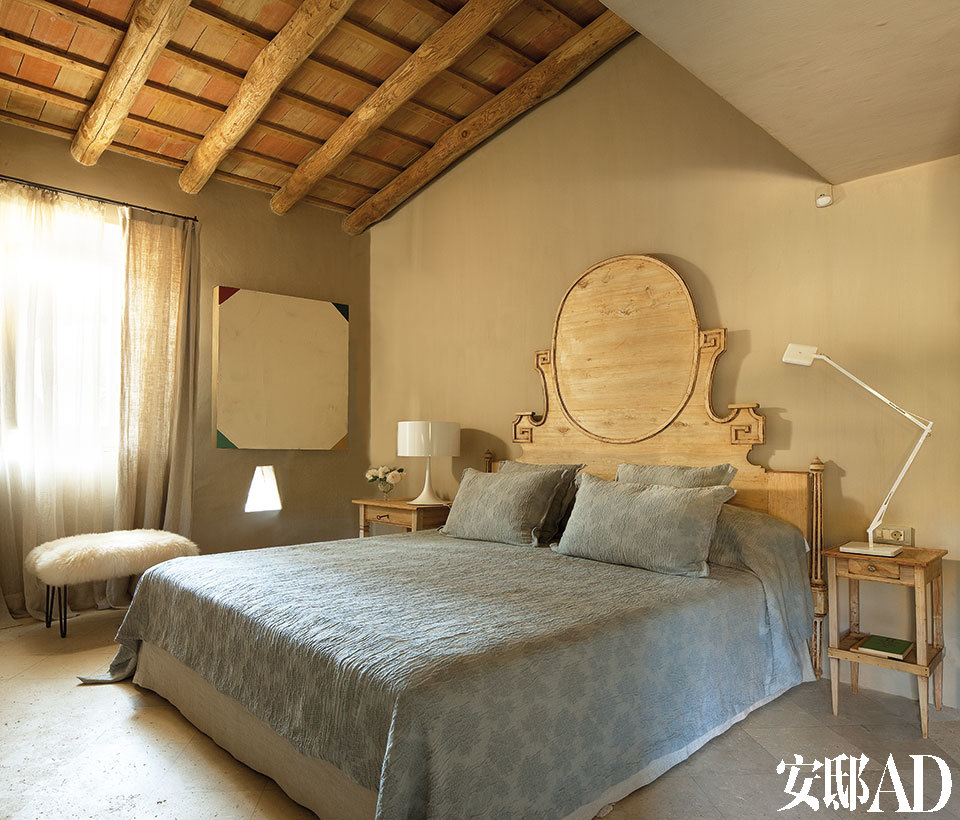 主卧室里，18世纪的床头为搭配睡床而进行了改造。亚麻床单来自Dominique Kieffer。床头柜的材质为欧洲山毛榉，是购于“Lucca”商店的古董商品。两盏白色床头灯均为Flos。羊毛凳子来自Serge Castella。墙上的画作来自艺术家Ballesteros。卧室的地面则为石灰岩材质。