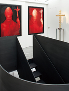 空间中的画廊部分。由Elliott亲手打造的黑钢打蜡楼梯无疑是其中的焦点。两块红色的画作是Andres Serrano的《红色的教皇》（Red Pope）。立在搁架上面的十字架来自Jean-Michel Othoniel。