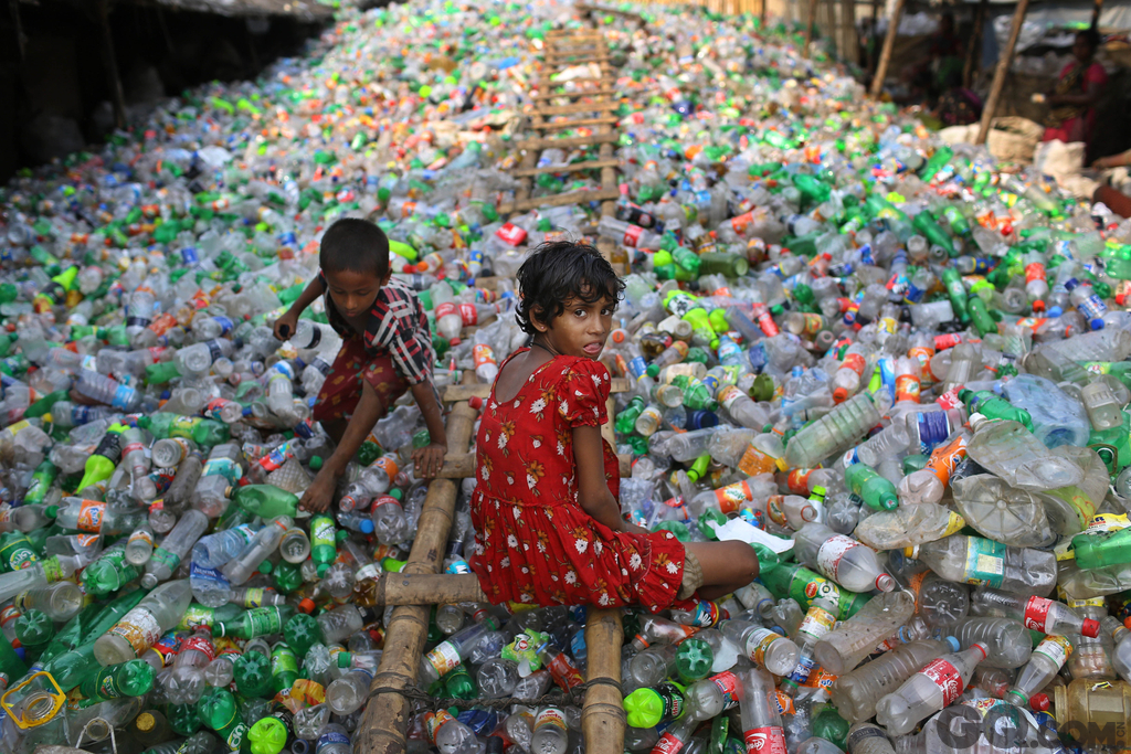 13岁的女孩Sharmin在塑料回收工厂里做工，一个小男孩在塑料瓶堆里玩耍。  
