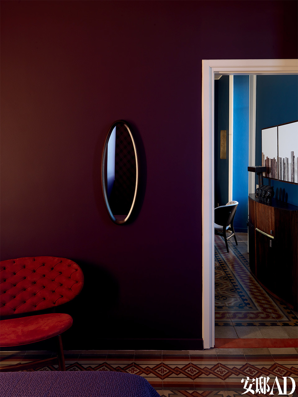 卧室与客厅相连的紫色墙面上，一面椭圆形古董镜，好像为整个空间添了一只神秘的眼睛。卧室里的墙面被漆成紫色，木框古董镜与来自Baxter的红色当代扶手椅和谐相处，呼应着地砖的红色，这里的视线能够望见客厅。