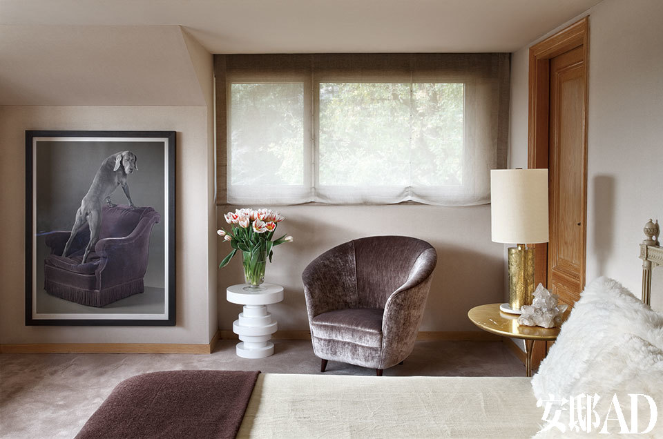 主卧，墙上的摄影作品出自艺术家William Wegman之手。放置鲜花的白色小凳来自Serge Castella Interiors，丝绒面扶手椅同样由Serge Castella Interiors设计。设计师Oppenheim设计的小桌上，摆放着一盏上世纪60年代的金色法国台灯。