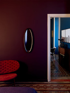 卧室与客厅相连的紫色墙面上，一面椭圆形古董镜，好像为整个空间添了一只神秘的眼睛。卧室里的墙面被漆成紫色，木框古董镜与来自Baxter的红色当代扶手椅和谐相处，呼应着地砖的红色，这里的视线能够望见客厅。