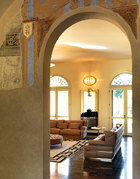 从走廊看向客厅，近处墙面上还部分保留着修复了的老壁画，客厅墙面上的椭圆形Benson壁灯由Samuele Mazza设计，壁灯下的装饰镜由Alessandro La Spada设计。